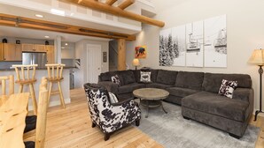 A modern living room with a sectional sofa, a round coffee table, and a wooden dining table with chairs. - True Ski-in/ski-out Saddle Ridge Townhome - private hot tub, new bathrooms (Big Sky)