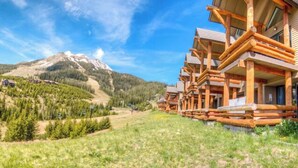 A row of log cabin-style lodges with a mountain backdrop. - True Ski-in/ski-out Saddle Ridge Townhome - private hot tub, new bathrooms (Big Sky)