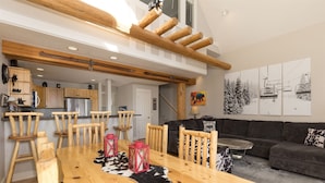 A spacious living area with a wooden dining table, a black and white cowhide rug, and a grey sofa. - True Ski-in/ski-out Saddle Ridge Townhome - private hot tub, new bathrooms (Big Sky)