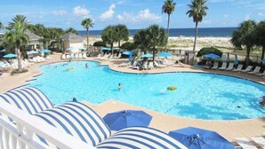 A pool area with lounge chairs and umbrellas, a beach view, and palm trees.