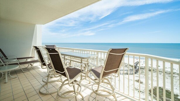 A balcony with a table and chairs overlooking a beach.