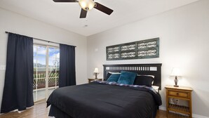 Quarto com cama, duas mesas de cabeceira, ventilador de teto e vista pela porta de vidro deslizante.