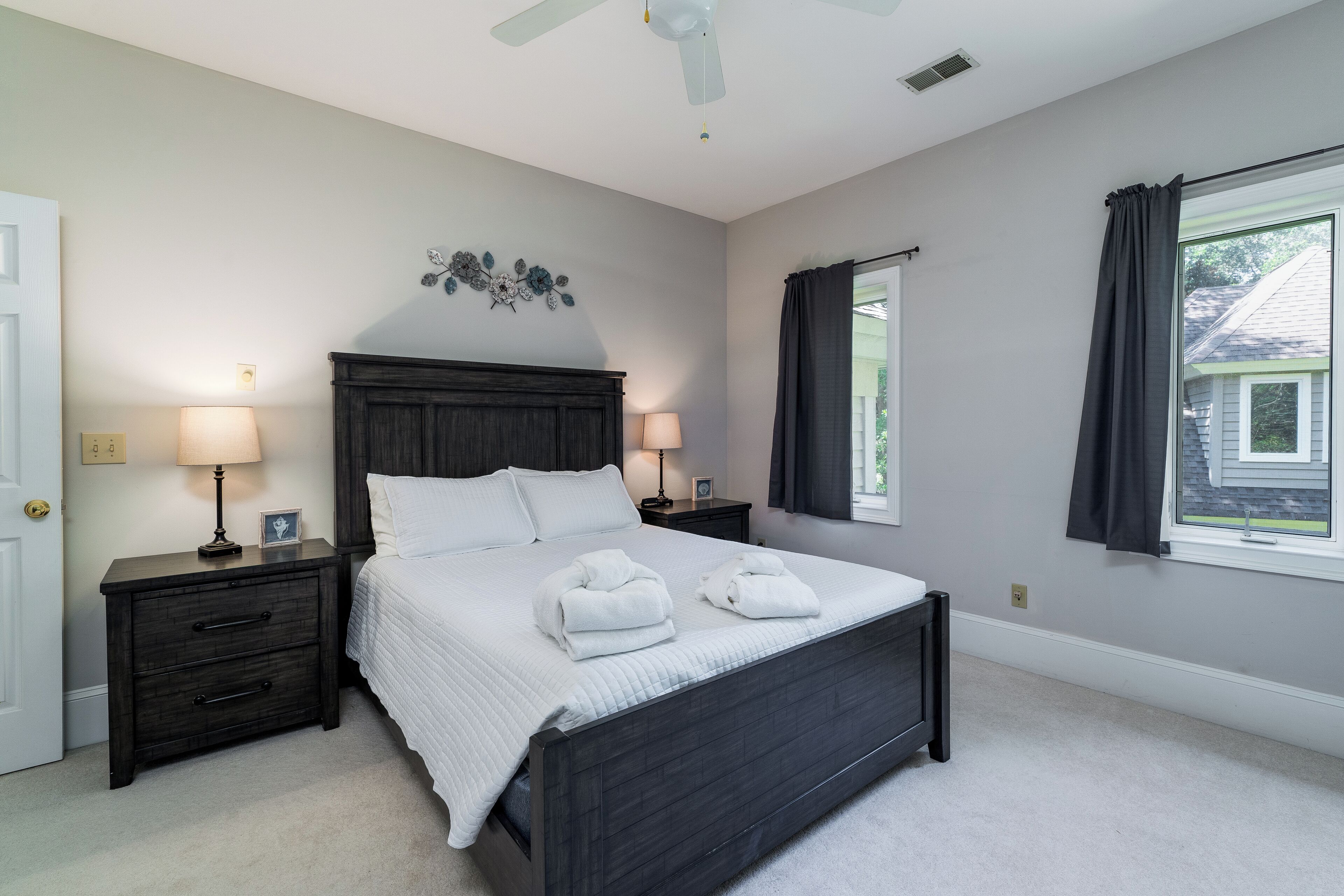 A bedroom with a large bed, two bedside tables, a ceiling fan, and a window with curtains.