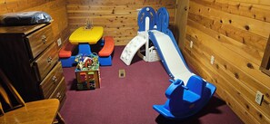 A children's play area with a slide, a small table, and a toy chest.