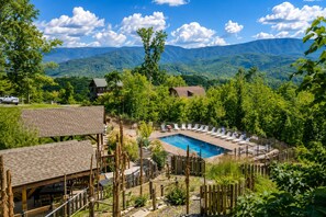 A pool area with lounge chairs, surrounded by a wooden fence and trees, with mountains in the background.