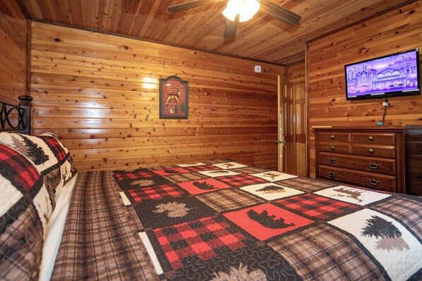 Una habitación tipo cabaña de madera con una cama, un aparador, un televisor y un reloj de pared.