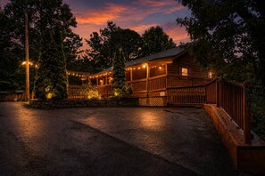 A wooden cabin with a porch, surrounded by trees, and illuminated by string lights.
