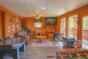 A cozy room with a pool table, foosball table, and a television mounted on the wall.
