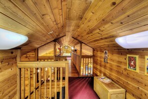 A wooden interior with a sloped ceiling, wooden railings, and a staircase leading to an upper level.