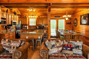 A cozy cabin interior with a kitchen, dining area, and seating with animal-themed cushions.