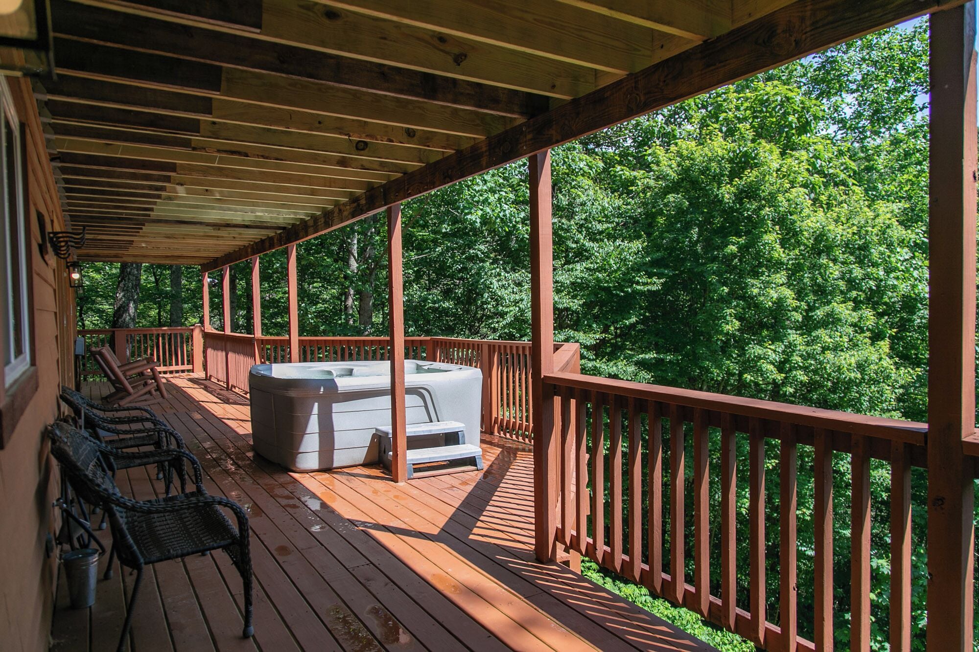 A wooden deck with a hot tub, lounge chairs, and a view of a forest.