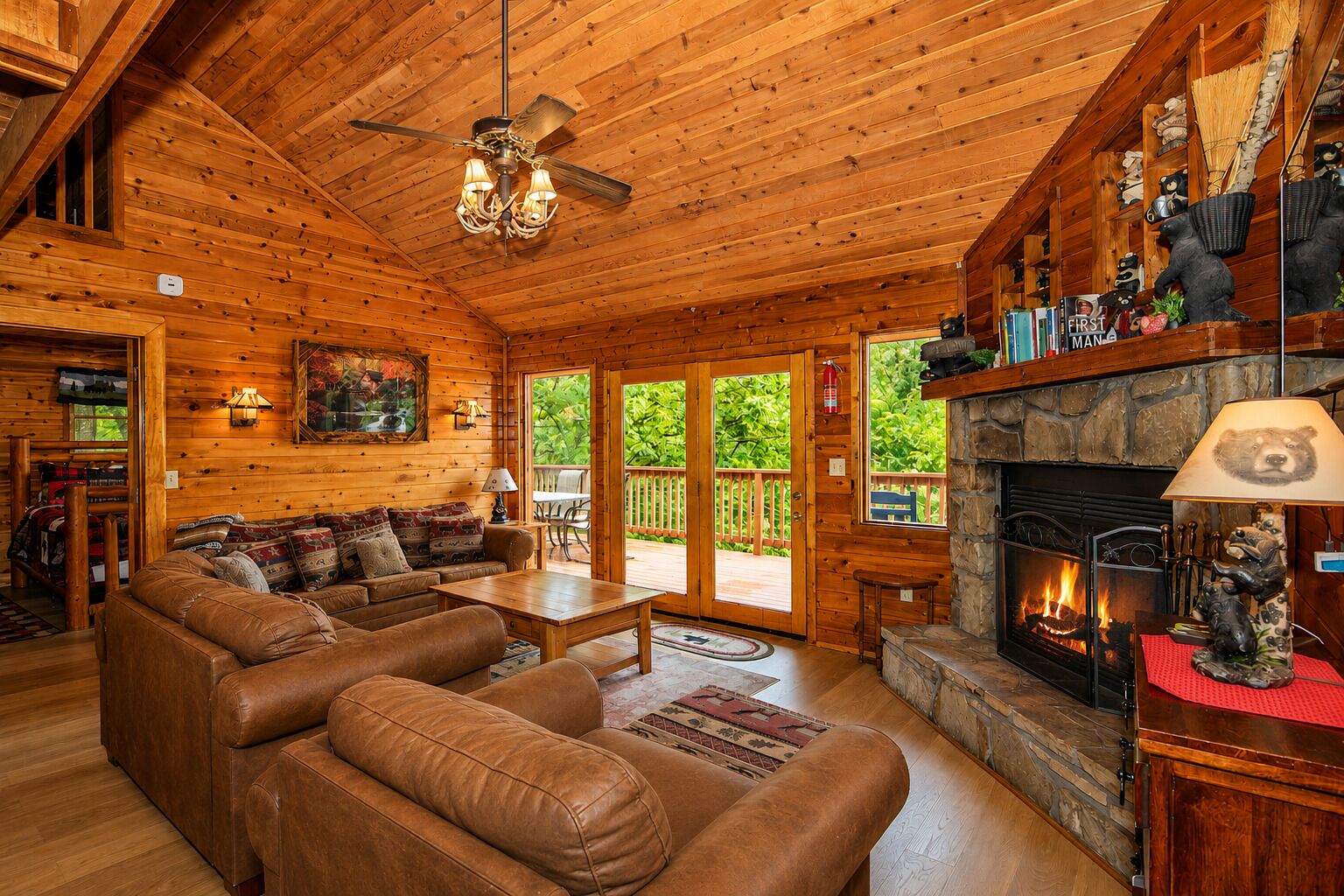 A cozy cabin interior with a fireplace, leather sofa, wooden ceiling, and a dining area.
