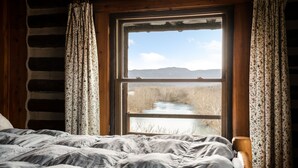 Ein Zimmer mit großem Fenster, Holzwänden und einem Bett mit grauer Decke.