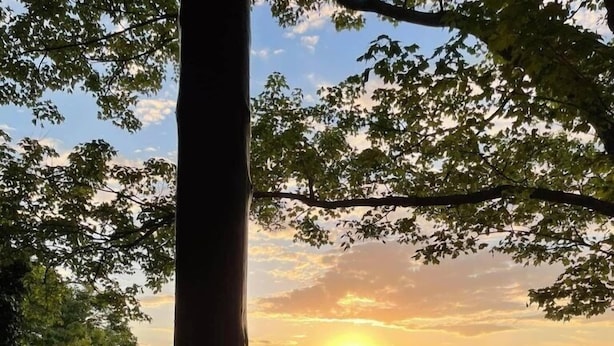 Blick von einem Holzbalkon auf einen Fluss und bewaldete Hügel bei Sonnenuntergang.
