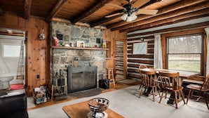 Ein rustikales Blockhaus-Interieur mit Kamin aus Stein, einem Holzespeisetisch und einem großen Fenster mit Blick ins Freie.