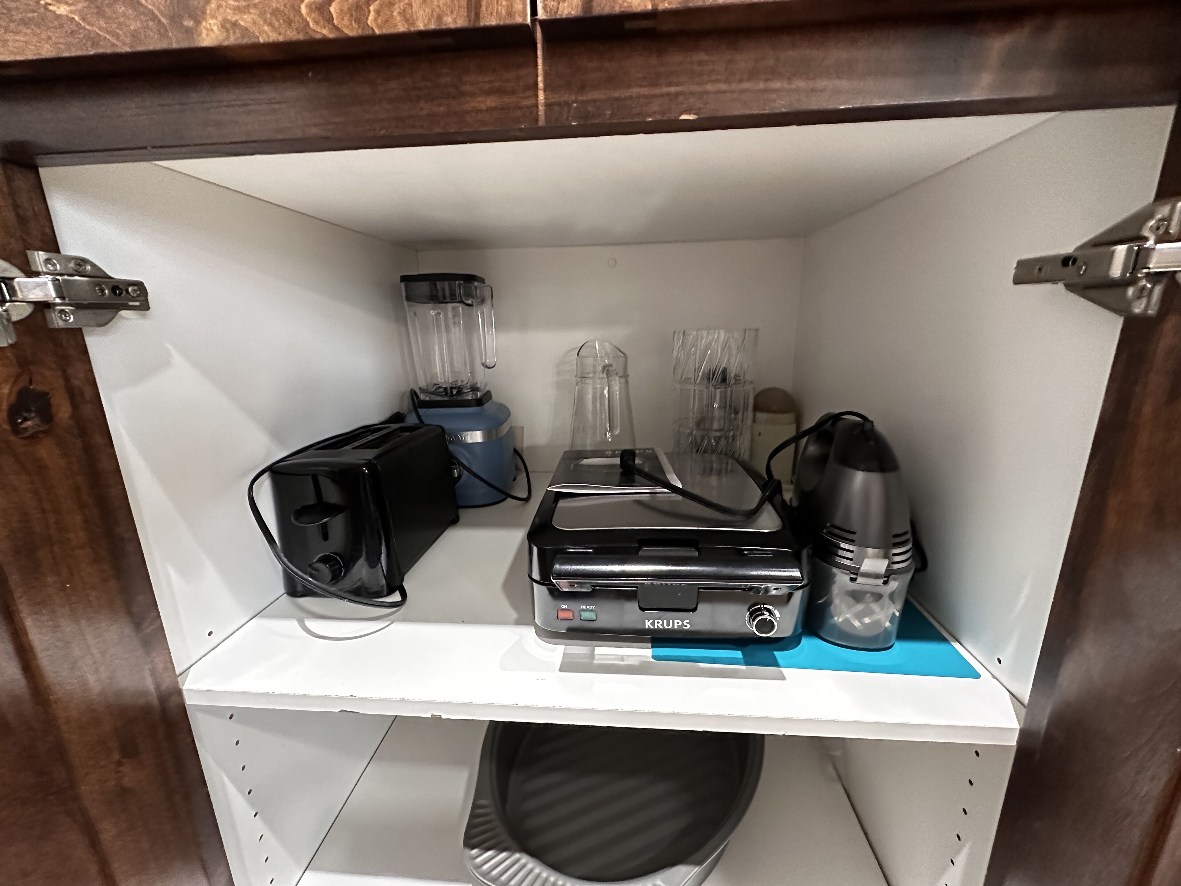 A kitchen shelf with a toaster, a blender, a coffee maker, and a Krups appliance.