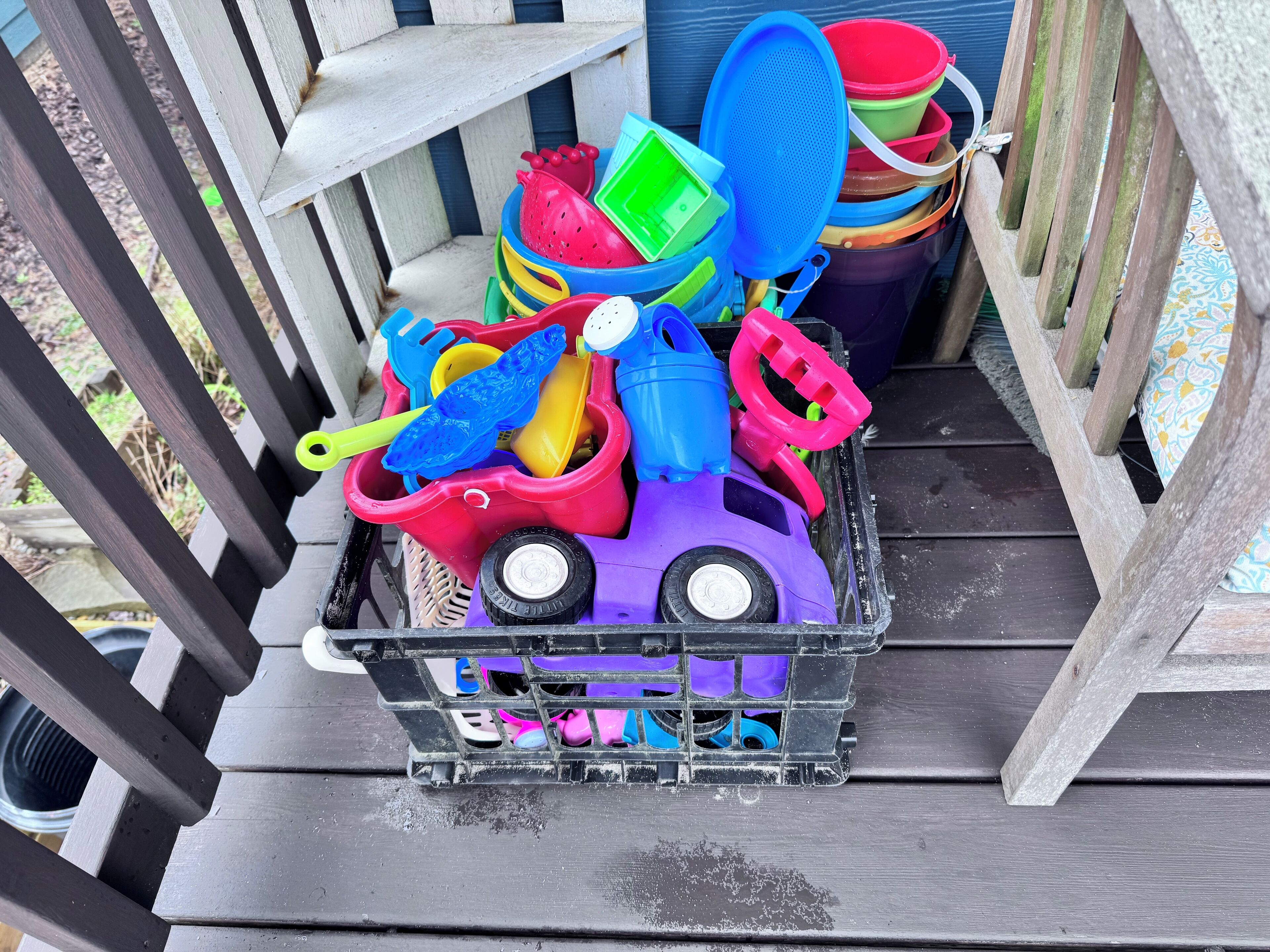 A plastic toy car filled with various colorful plastic containers and utensils on a wooden deck.