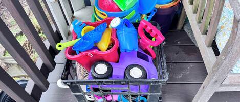 A plastic toy car filled with various colorful plastic containers and utensils on a wooden deck.