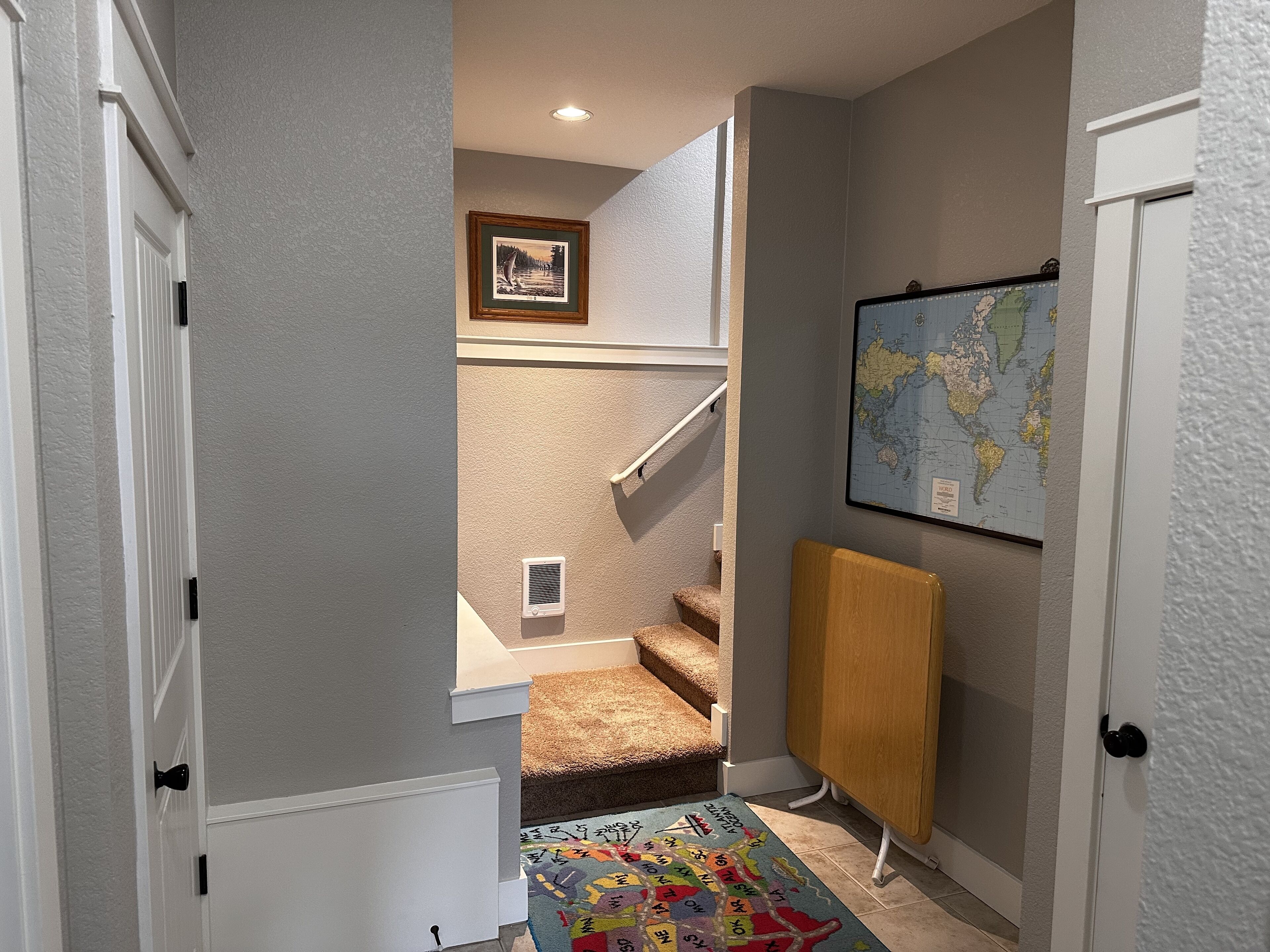 A hallway with a carpeted staircase, a framed picture above the stairs, and a world map on the wall.