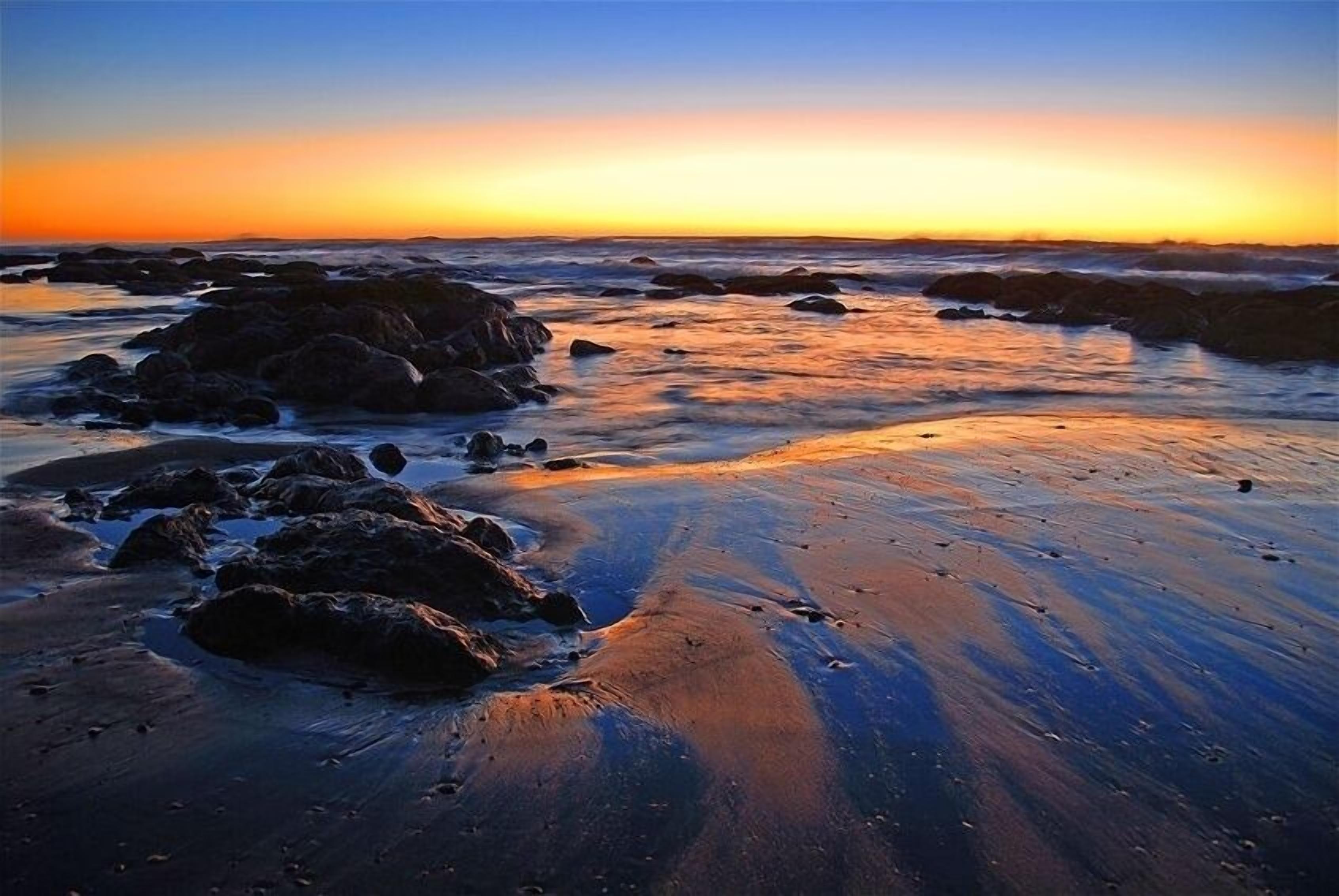 A beach with rocks and water at sunset.
