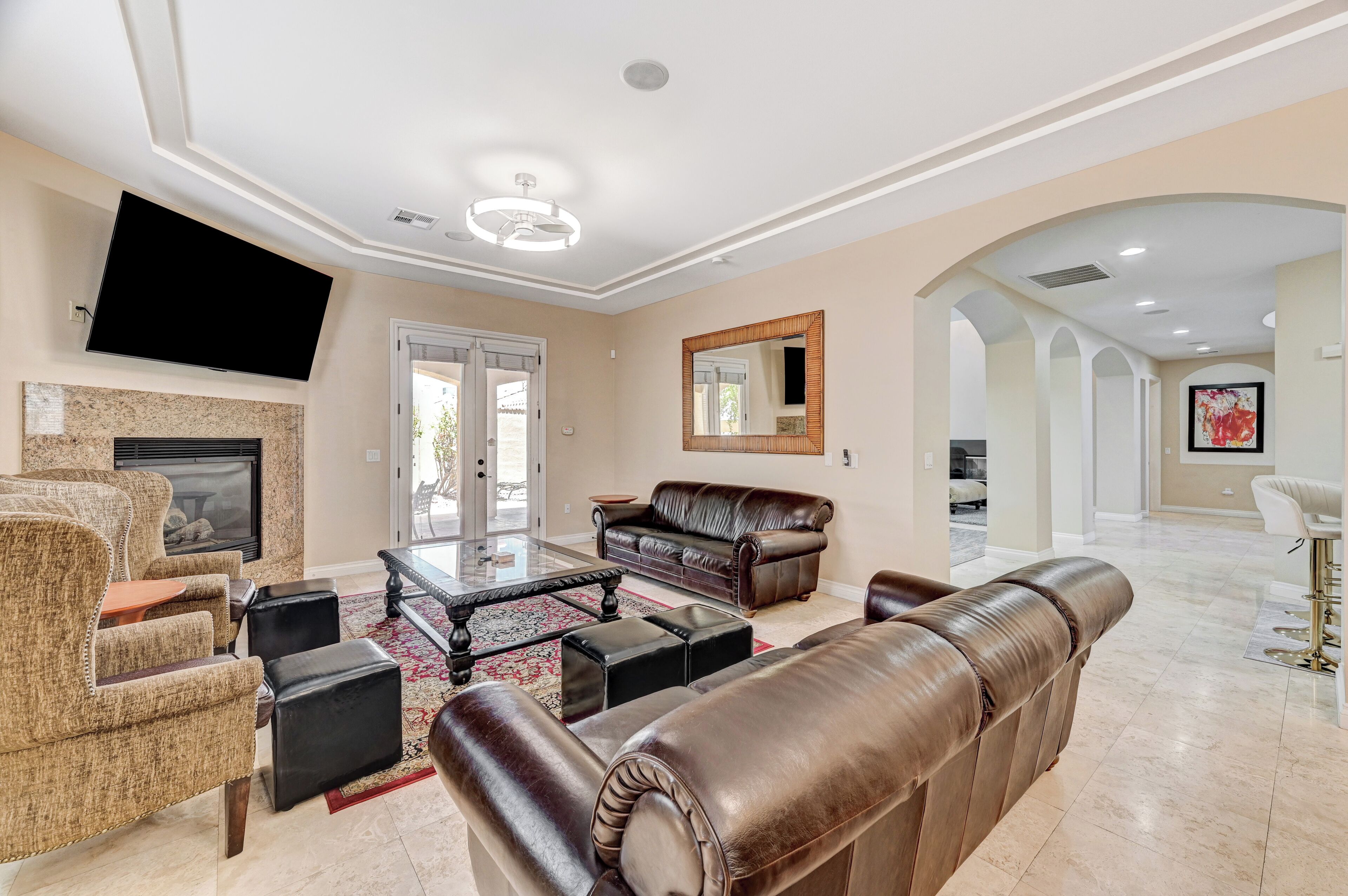 A spacious living room with a fireplace, leather sofas, a flat-screen TV, and a large mirror.