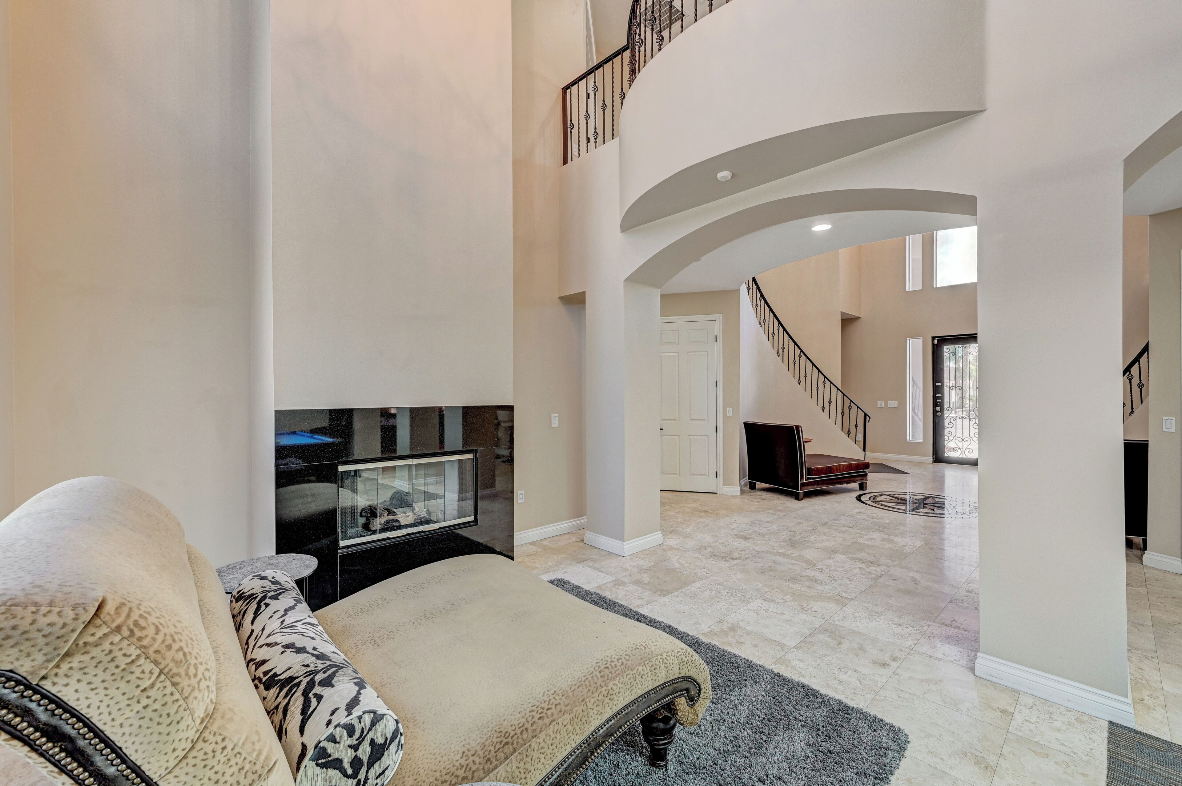 A spacious living area with a high ceiling, a staircase, and a modern fireplace.