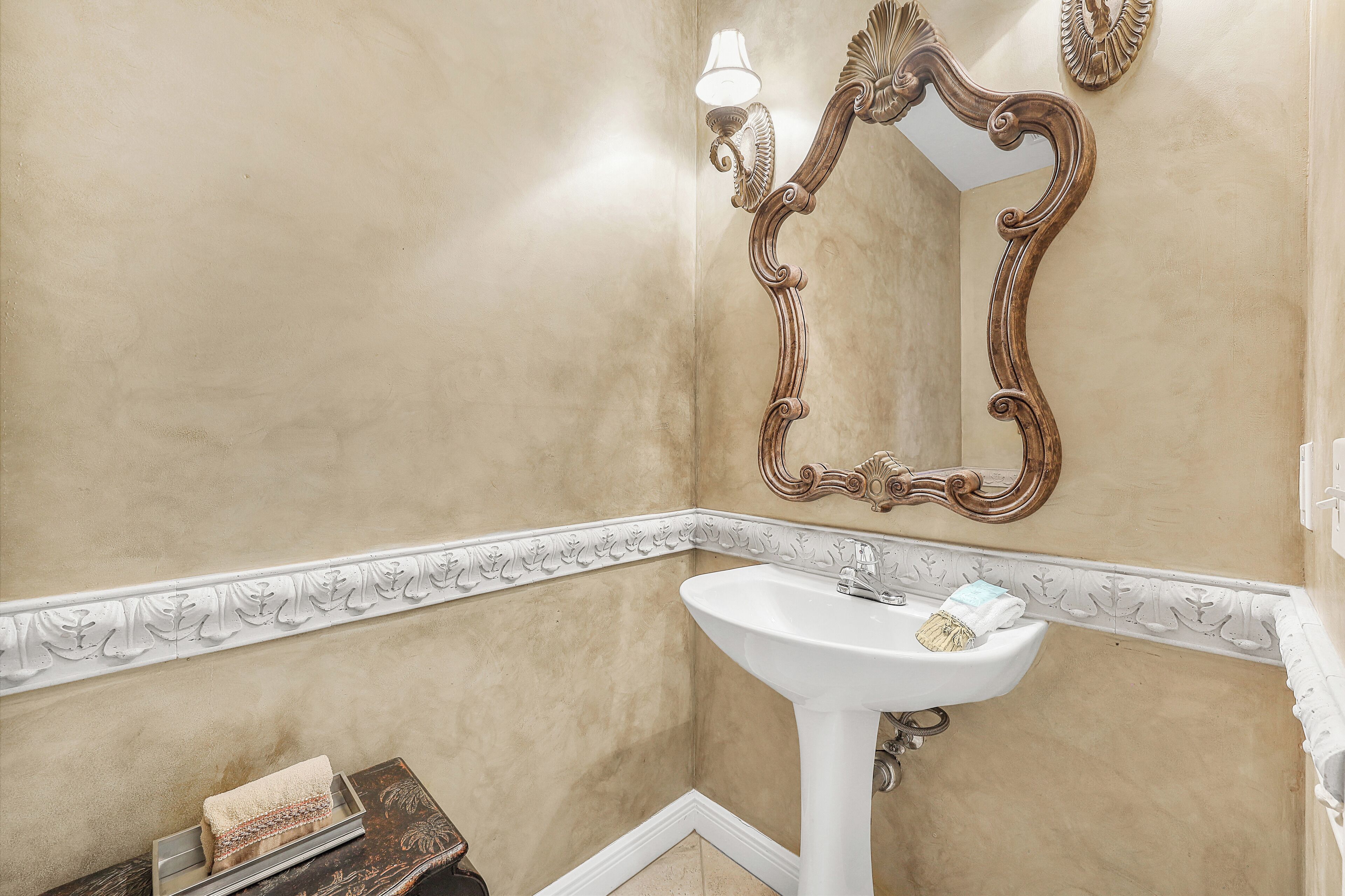 A bathroom with a white pedestal sink, a mirror with an ornate frame, and a towel rack with a towel.