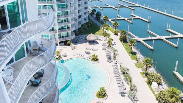 A high-rise hotel with a large pool, multiple balconies, and a marina with docks.