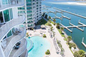 A high-rise hotel with a large pool, multiple balconies, and a marina with docks. - Caribe D903 Luxury Condo- Amazing Views, Lazy River, Pools & Beach Access (Orange Beach)
