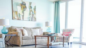 A living room with a sofa, coffee table, and chairs, a painting on the wall, and a large window with curtains.