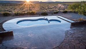 Ein Pool mit ungewöhnlicher Form, umgeben von einer Steinterrasse und einer Wüstenlandschaft mit einem Berg im Hintergrund.