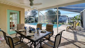 A covered patio with a pool view, outdoor seating, and a ceiling fan.