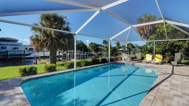 A swimming pool with a covered area, surrounded by palm trees and a herringbone-patterned patio.