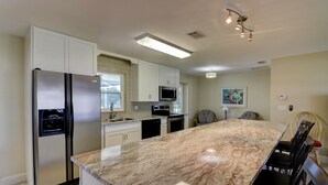 A modern kitchen with a large island, stainless steel appliances, and a dining area with chairs.