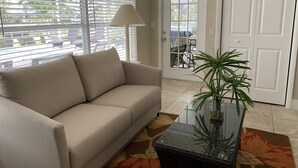A living room with a beige sofa, a glass coffee table with a plant, and a patterned rug.