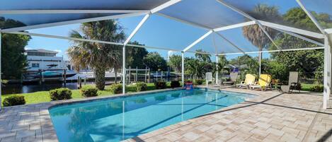 Una piscina coperta con superficie d'acqua blu trasparente, circondata da un solarium lastricato e una struttura a tettoia bianca.