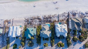 Vista aérea de una propiedad frente a la playa con varias casas, una playa de arena y un océano azul claro.