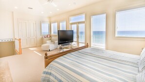 Un dormitorio con una cama grande, televisión y vista al mar desde las ventanas.