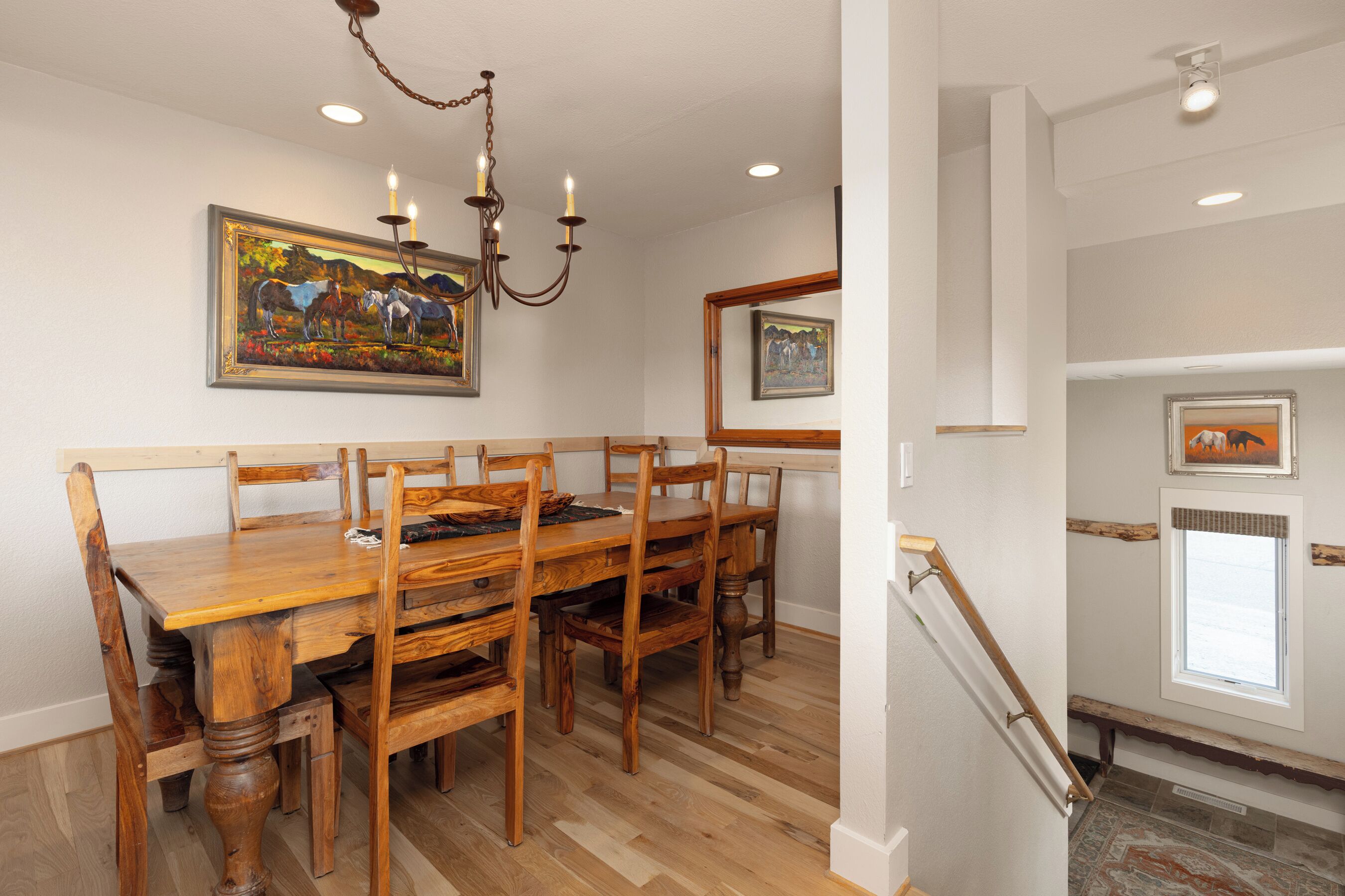 A dining area with a wooden table and chairs, a chandelier, and framed artwork on the walls.