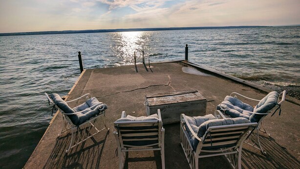 A concrete pier with four white lounge chairs facing a calm body of water. - Charming Cottage  LITERALLY on  Lake --Pet Friendly with Guest Cottage (Romulus)