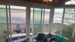 A sunroom with large windows overlooking a lake, furnished with chairs, a table, and a sofa. - Charming Cottage  LITERALLY on  Lake --Pet Friendly with Guest Cottage (Romulus)