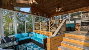 A cozy interior with a wooden ceiling, large windows, a blue sofa, and a staircase leading to an upper level. - Charming Cottage  LITERALLY on  Lake --Pet Friendly with Guest Cottage (Romulus)