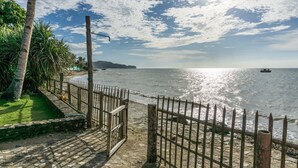 A coastal walkway with a wooden fence, a stone pathway, and a view of the sea with boats. - HangOut Beach & Resort (Malay)