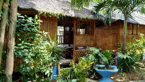 A thatched-roof hut with a wooden porch, surrounded by lush tropical plants. - HangOut Beach & Resort (Malay)