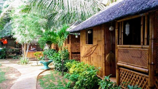 A bamboo structure with a thatched roof, surrounded by lush greenery and a stone pathway. - HangOut Beach & Resort (Malay)