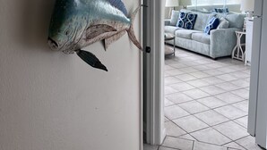 Un saló amb un peix gran penjat a la paret, un sofà amb coixins i una porta que dona a una altra habitació.