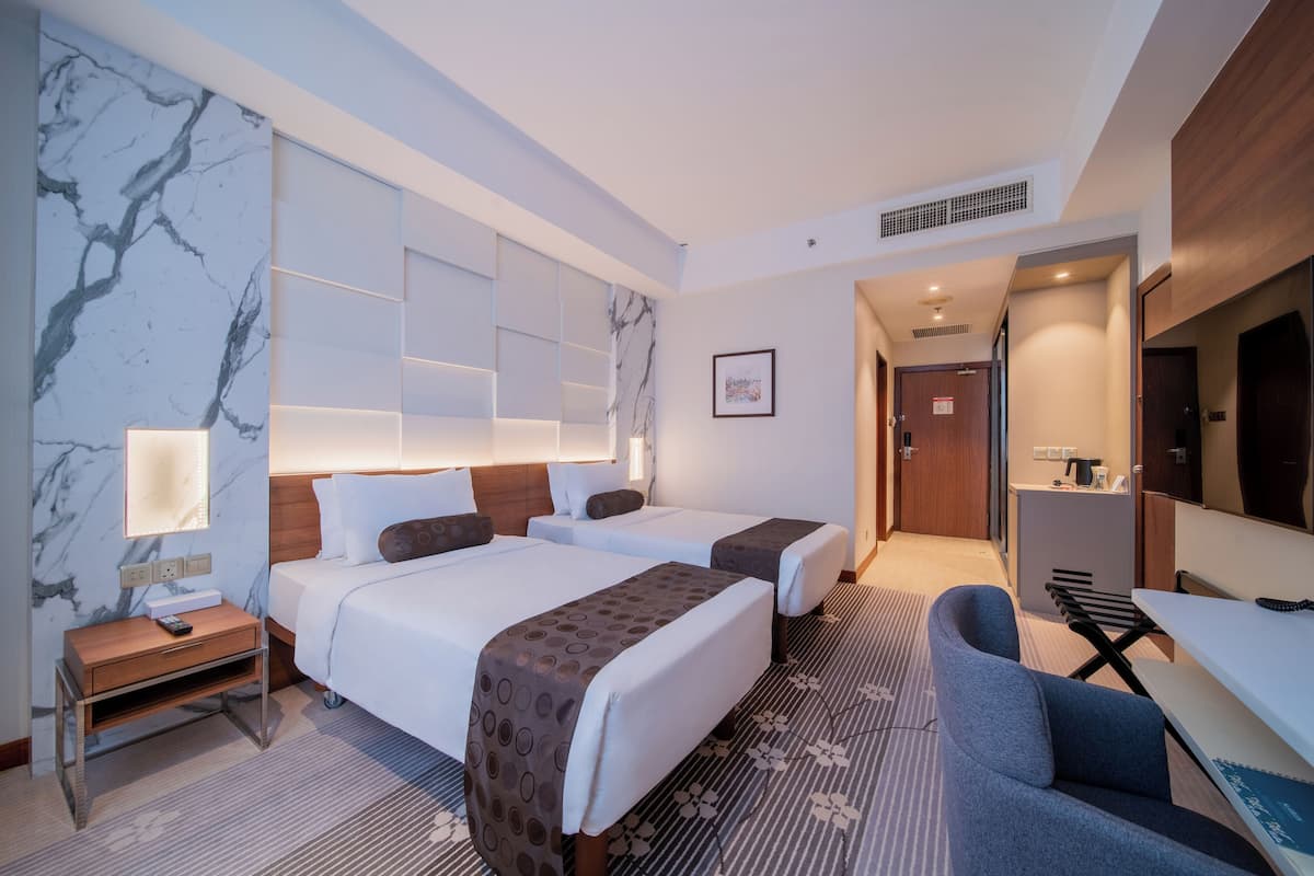 Une chambre d’hôtel avec deux lits, un bureau, une chaise, une télévision et une salle de bain visible à travers une porte ouverte.