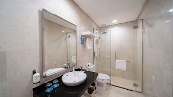 Un baño moderno con un espejo grande, un lavamanos, un inodoro y una ducha con mampara de vidrio.