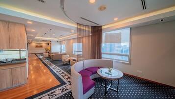 A modern hotel room with a curved white sofa, a round table, and a large window offering a city view.
