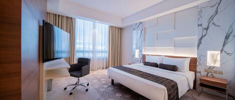Una habitación de hotel moderna con una cama grande, un escritorio, una silla y un televisor.